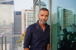 © phocal Media - Portrait of Expat man leaning on glass window at balcony.