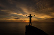 © yingtanthawarak - silhouette of woman hand up and standing on rock in sunset.