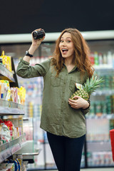 Wall Mural - Smiling young casual woman with shopping cart looking at products