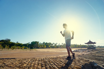 Wall Mural - Sports lifestyle. Happy young african man jogging on the sea shore.