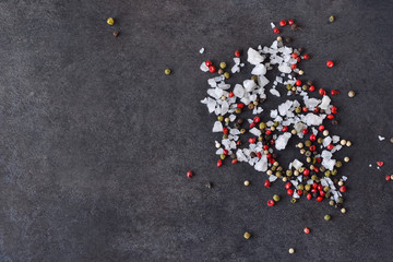 Black food background with spices. A mixture of peppers and salt on shale stone. Top view.