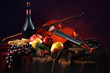 Violin with a bow on a red background next to a bottle of old wine and wet fruit