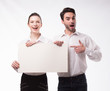 © yanushkov - Young happy couple showing presentation pointing on placard over gray background