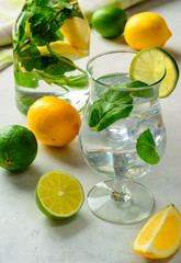 Homemade refreshing summer lemonade in a glass with lime, lemon and mint on a white concrete or stone  background.