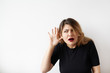 © shurkin_son - Portrait of funny plus size young woman looking aside holding hand to her ear and trying to hear something standing on white background. Cute Caucasian female with a hearing disorder or hearing loss