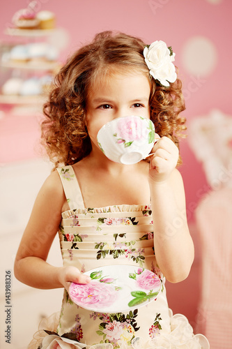 Little Cute Girl In A Pink Dress Drinks Tea With Sweets In The