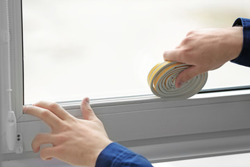 Hands of young worker applying rubber strip onto window in office