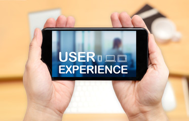 Poster - Watching two hand holding mobile phone with user experience word on screen and blur desk office background,Digital marketing concept