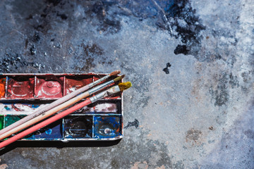 Old used watercolor set and old brushes on grunge metal background. With space for text