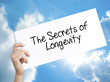 The Secrets of Longevity Sign on white paper. Man Hand Holding Paper with text. Isolated on sky background