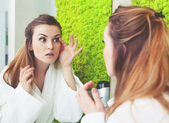 Sticker - Pretty woman looking at mirror in modern bathroom and checking wrinkles