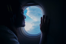 A Beautiful Asian Woman Looking Through An Airplane Window With Clouds And Sky Background