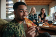 Man eating slice of pizza while hanging out with friends