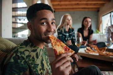 Wall Mural - Man eating slice of pizza while hanging out with friends