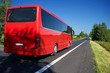 The red bus traveling on asphalt road lined avenue of trees in a rural landscape on a bright sunny day