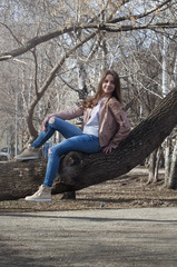 The beautiful Russian girl with long hair sits on a tree and smiles.