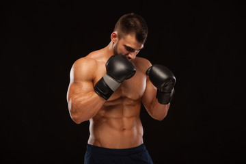 Muscular young man with perfect Torso with six pack abs, in boxing gloves is showing the different movements and strikes isolated on black background with copyspace