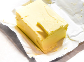 Creamy butter in its unwrapped foil paper. Isolated on light table