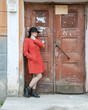 © Dmitriy - Young beautiful girl dressed in red coat posing near an old door from the entrance of the house. Female face in shadow.