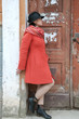 © Dmitriy - Young beautiful girl dressed in red coat posing near an old door from the entrance of the house. Female face in shadow.