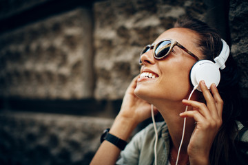 Wall Mural - Happy young woman listening to music via headphones on the street on a sunny day