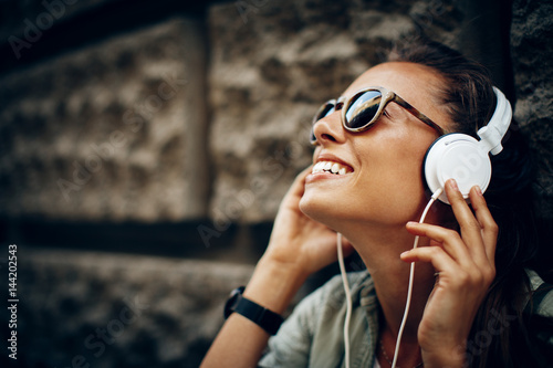 Photographie Happy young woman listening to music via headphones on the street on a sunny day