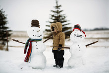 Boy Standing By Snowmen On Field Against Sky
