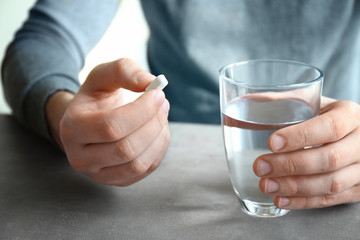 Young man with pill and glass of water at home, closeup