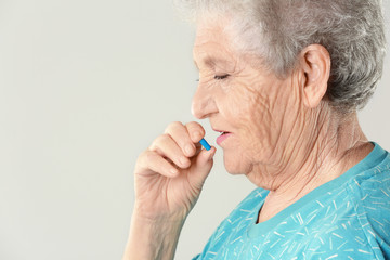 Poster - Elderly woman taking pill on light background