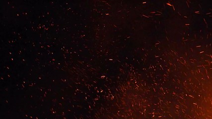 burning ash rise from large fire in the night sky.