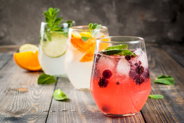 Wall Mural - Selection of three kinds of gin tonic: with blackberries, with orange, with lime and mint leaves. In glasses on a rustic wooden background. Copy space 