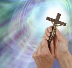 Praying to Our Lord - Female hands gently holding a Crucifix of Jesus Christ up towards a ball of light on a green blue purple radiating light background with copy space on the left 
