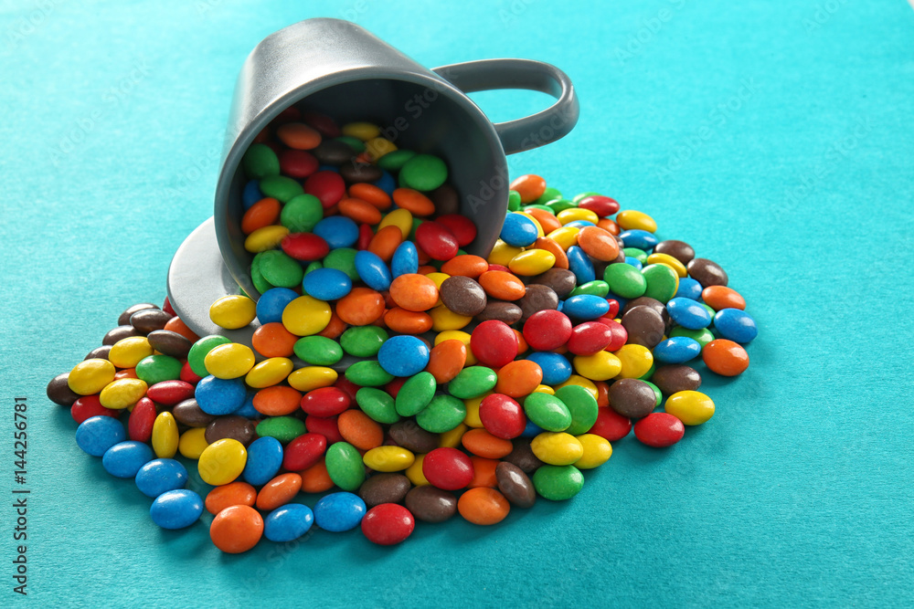 Delicious colorful candies and cup on color background