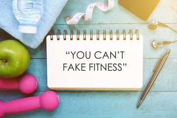 Fitness motivation quotes written on open notebook. Fitness equipment on wooden background.