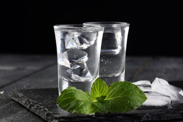 Vodka in shot glasses and ice on rustic wood background