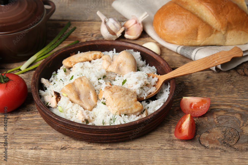 Bowl with tasty chicken and rice on wooden table