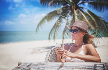 Young beautiful woman with mobile phone on the shore of the tropical sea in a cafe. Communication and internet in travel concept