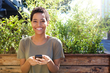 Wall Mural - smiling african american woman holding mobile phone outdoors