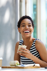 smiling young woman eating sandwich outside