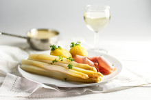 Juicy White Asparagus Dish With Potatoes And Ham On A White Plate, Sauce Hollandaise And Wine Blurred In The Bright Background, Copy Space