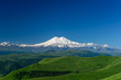 Great nature mountain landscapes. Fantastic perspective of caucasian snow inactive volcano Elbrus with green fields and road to it and clearly blue sky background. Russia