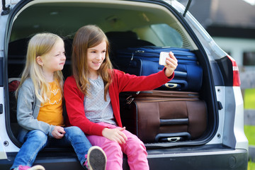 Two adorable little sisters taking photo of themselves before going on vacations with their parents