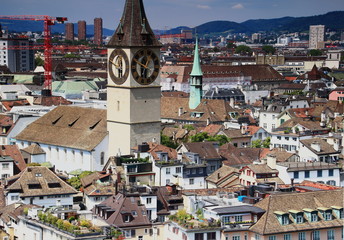 Cityscape of Zurich city center: old town rooftops and the reformed St. Peter Church with the largest clock in Europe in a sunny summer day, from Grossmunster cathedral, Switzerland