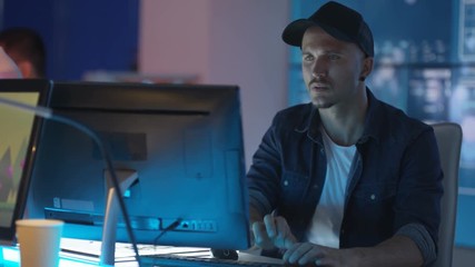  Young creative computer game designer working with colleagues in dark office. 