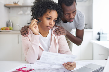 African american female analyzing unpaid bills with her supporting husband, looking at laptop screen, using online bank application. Young bankrupt couple have Financial problems. No money concept