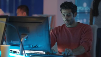  Young creative computer game designer working with colleagues in dark office. 