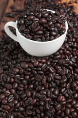 Wall Mural - Close up shot of dark roasted coffee bean in white ceramic cup on wooden floor with copy space