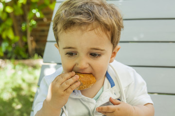 Close up portrait baby boy eating bread in the garden