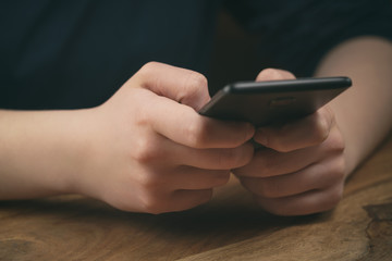 Wall Mural - young female teen hands using smatphone sitting at the table closeup, shallow focus