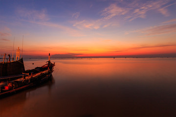 Sunset over sea shore and silhouette shell farm with fishing boat